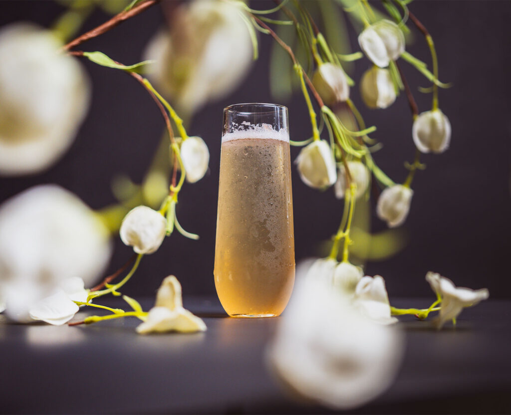 The Hummingbird cocktail in a champagne flute, surrounded by white flowers