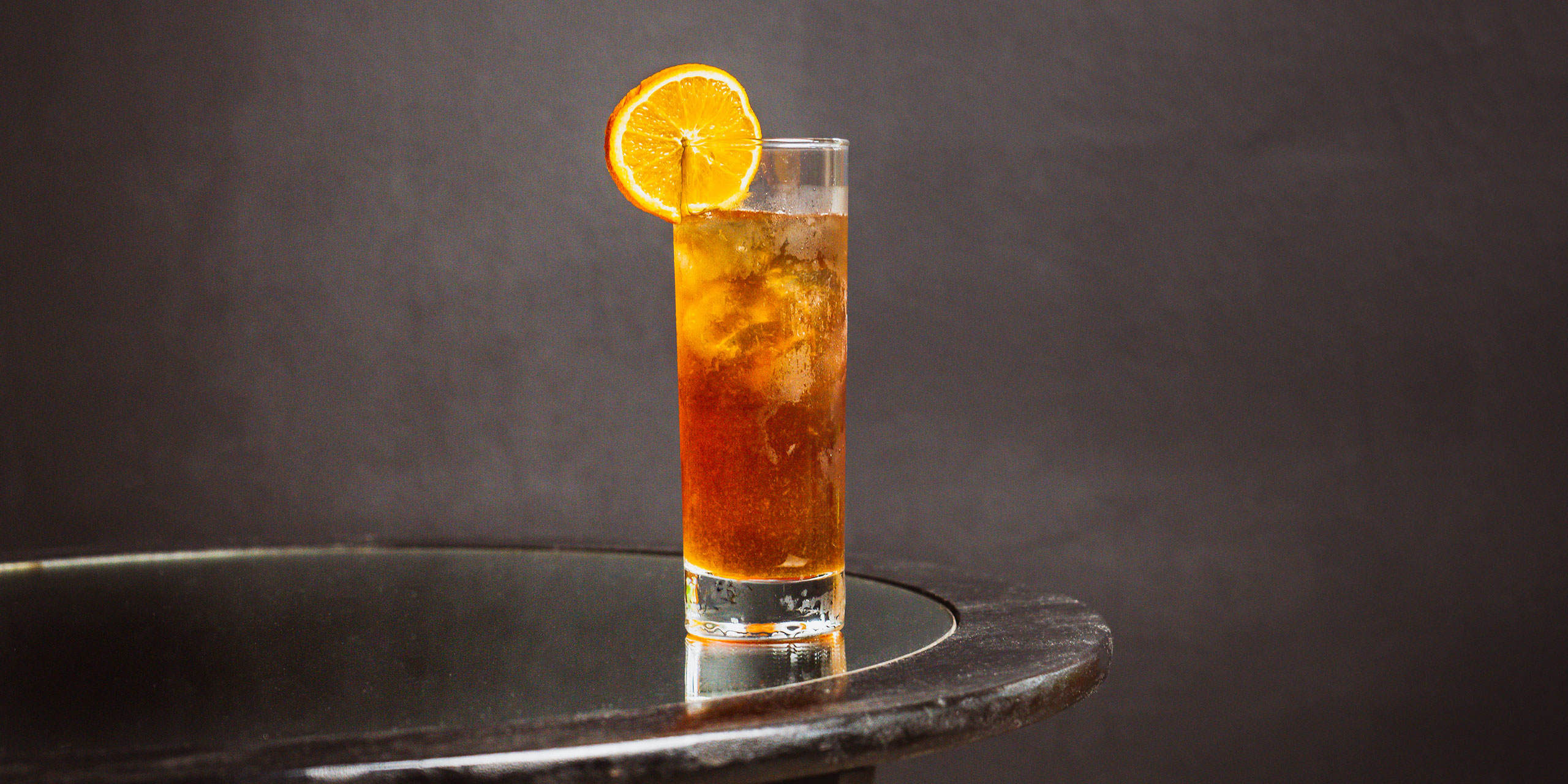 Vermouth Swizzle with an orange garnish on a mirrored table