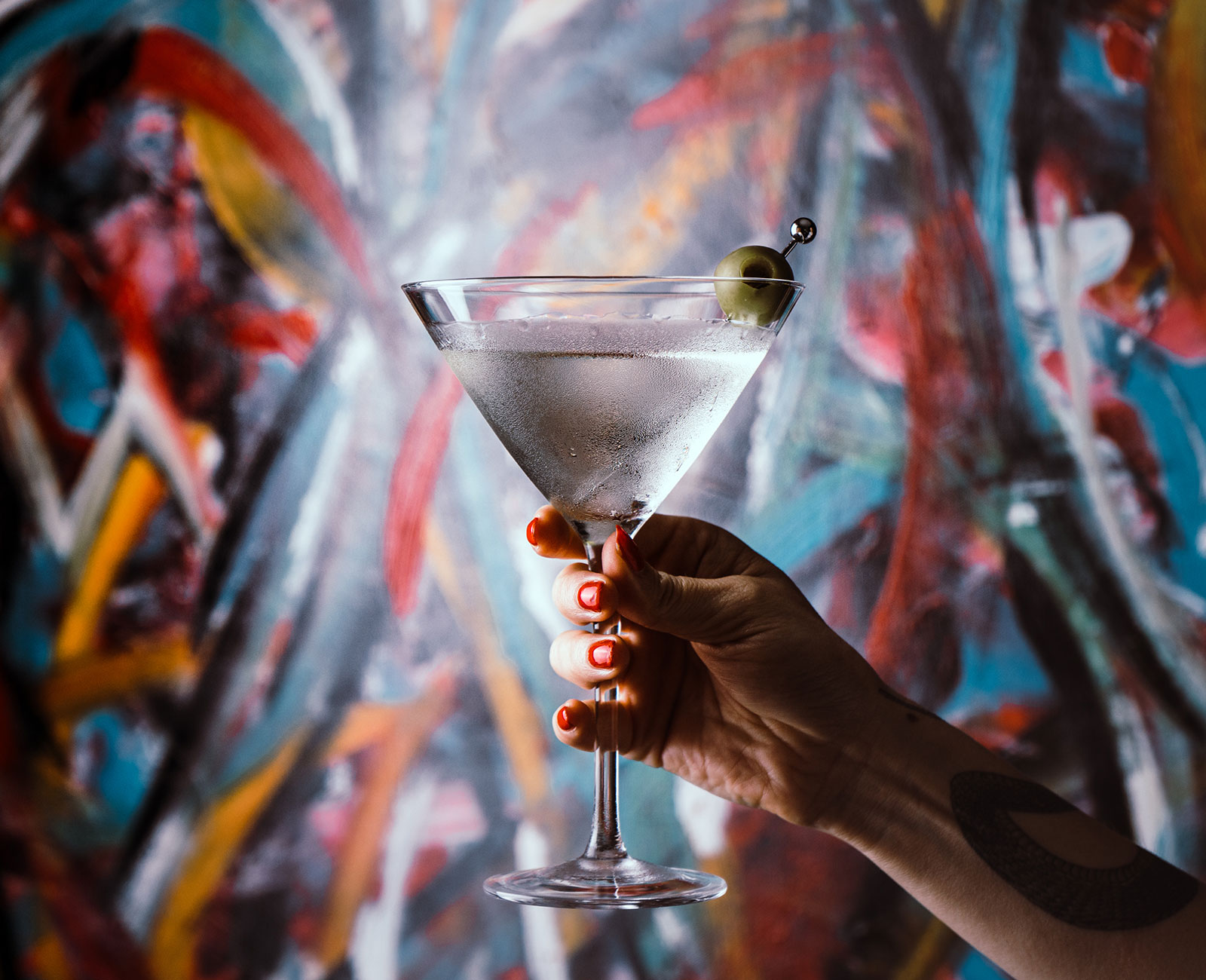 Vya Whisper Dry Vodka Martini with an olive garnish and a painting in the background